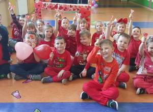 Grupa Zuchy - zdjęcie grupowe przedszkolaków siedzących siadem skrzyżnym w czerwonych strojach a w dłoniach trzymają serduszka.