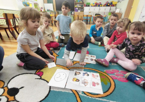 Przedszkolaki siedzą na dywanie i segregują emocje na przyjemne i nieprzyjemne.