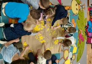 Kamyczki na dywanie wyklejają duże słońce dedykowane dla osób które potrzebują pomocy.