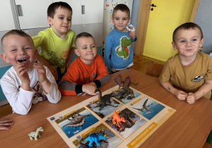 Chłopcy z grupy Promyczki układają dinozaury na planszy edukacyjnej.