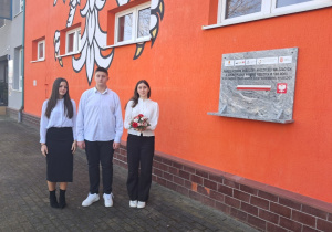 Delegacja uczniów z kl. VII a i VIII a przed budynkiem szkoły z kwiatami obok tablicy upamiętniającej poległych w walce o szkołę polską.