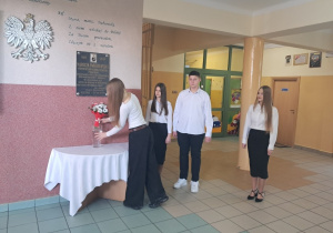 Przewodnicząca składa kwiaty pod tablicą Narcyzy Żmichowskiej na szkolnym korytarzu obok stoi delegacja uczniów z klasy VIII a i VIII b.