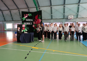 Uczennice klasy IV przedstawiają scenkę z Narcyzą Żmichowską , przebrana uczennica siedzi przy stoliku odpowiada na pytania koleżanek.