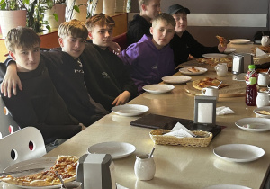 Uczniowie jedzą pizzę i rozmawiają.