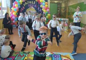 Chłopcy z grupy Skoczki i Zuchy w ciemnych okularach, koszulach i szelkach rozpoczynają swój układ taneczny z okazji Dnia Kobiet.