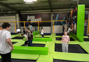 Uczniowie skaczący na trampolinach, w prawym górnym rogu uczennice skaczą i grają w gry zręcznościowe.