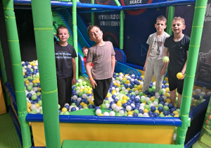 Uczniowie korzystający ze zjeżdżalni do basenu z kulkami.