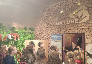 Grupa uczniów przy wystawie o tematyce biologicznej.