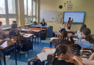 Uczennice klasy VIII prowadzą zajęcia matematyczne w klasie V przy tablicy uczennica rozwiązuje zadanie.