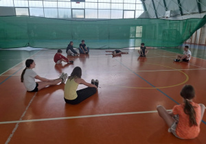 Uczniowie klasy VIII a prowadzą zajęcia w-f z klasą V robią na hali ćwiczenia w pozycji siedzącej.