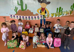 Przedszkolaki z Grupy Kamyczki i Promyczki prezentują swoje „ oryginalne plecaki” na dywanie.