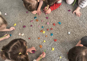 Szkraby podnoszą z dywanu motylki za pomocą słomki.