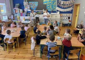 Pani Klaudia Wójciak przedstawia się dzieciom z grupy Promyczki, opowiada o swojej pasji do cukiernictwa, dzieci siedzą przy stolikach.