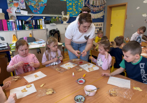 Pani Klaudia pomaga przedszkolakom dekorować ciasteczka lukrowymi mazakami.