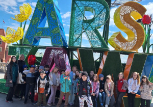 Uczniowie klasy pierwszej ze Szkoły Podstawowej w Rzeczycy wraz z wychowawcą i opiekunem stoją przed napisem Warszawa.