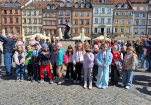 Uczniowie klasy pierwszej z Rzeczycy znajdują się na Rynku Starego Miasta i pozują do zdjęcia przed Syrenką Warszawską.