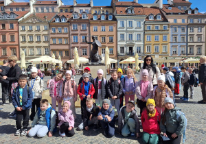 Uczniowie klasy pierwszej z Sadykierza znajdują się na Rynku Starego Miasta i pozują do zdjęcia przed Syrenką Warszawską.