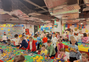 Dzieci z zaangażowaniem i pomysłowością budują z klocków lego.