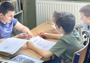Uczniowie Szkoły Podstawowej w Rzeczycy rozwiązują krzyżówki w bibliotece.