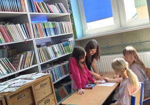 Uczennice Szkoły Podstawowej w Rzeczycy rozwiązują krzyżówki w bibliotece.