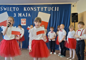 Dziewczynki trzymają w ręku flagę i pięknie recytują wiersze podczas apelu.