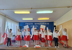 Uczniowie trzymają w ręku wysoko uniesioną wstążkę białą podczas tańca.