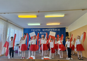 Uczniowie podczas tańca trzymają w ręku wysoko uniesioną czerwoną wstążkę.