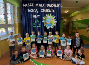 Zdjęcie grupowe grupy Promyczki, dzieci trzymają w dłoniach planetę Ziemia malowaną farbami za pomocą patyczków kosmetycznych.