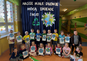 Zdjęcie grupowe grupy Promyczki, dzieci trzymają w dłoniach planetę Ziemia malowaną farbami za pomocą patyczków kosmetycznych.