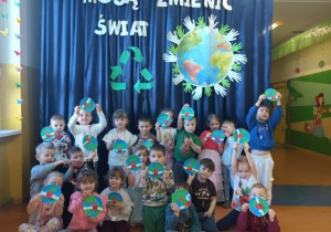 Zdjęcie grupowe dzieci z grupy Szkraby na tle dekoracji "Nasze małe dłonie mogą zmienić świat".