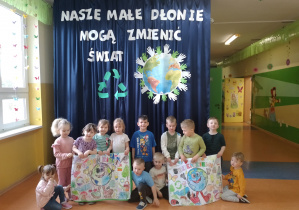 Zdjęcie grupowe dzieci z grupy Kamyczki na tle dekoracji "Nasze małe dłonie mogą zmienić świat".