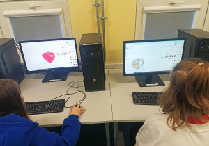 Uczniowie siedzą przy komputerach. Na monitorach widoczne są trójwymiarowe modele serduszek.